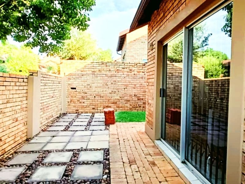 A private rear courtyard featuring a face brick boundary wall, paved patio area, and a large sliding glass door providing access to the home.