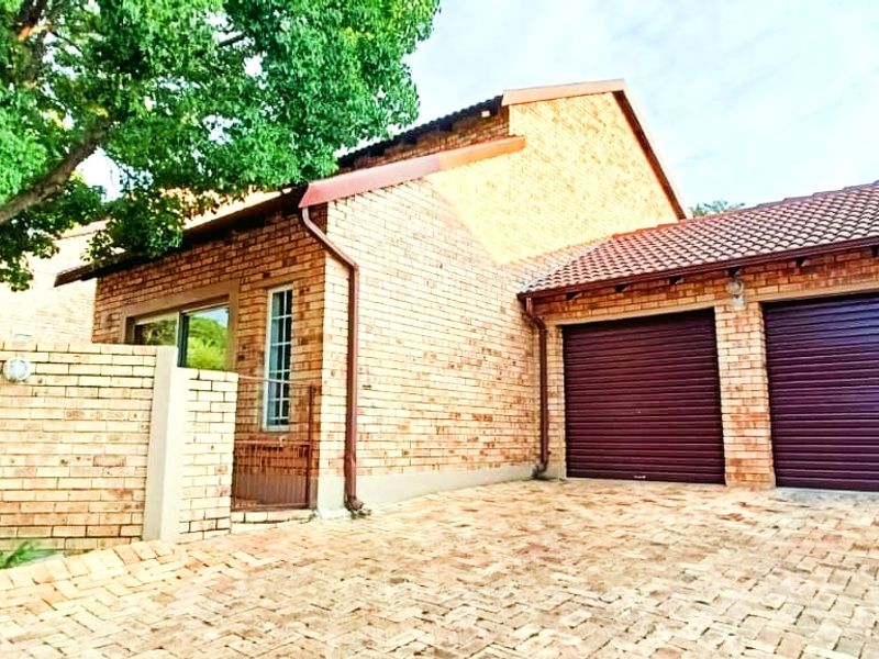 Front exterior view of a face brick townhouse featuring a double garage with roller shutter doors and a paved driveway.