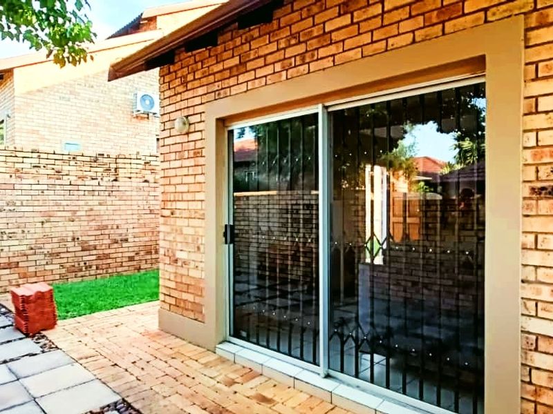 Rear exterior view of the townhouse featuring a face brick facade, paved patio area, and sliding glass door with security gate.