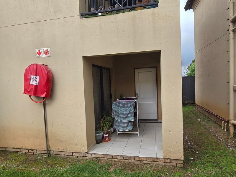 Rear exterior view of the apartment building featuring a small tiled patio area, fire safety equipment, and external drainage infrastructure.