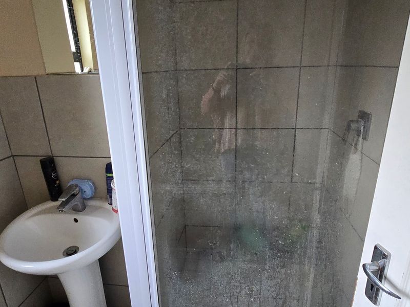 A compact bathroom featuring a pedestal basin and a shower enclosure with tiled walls.