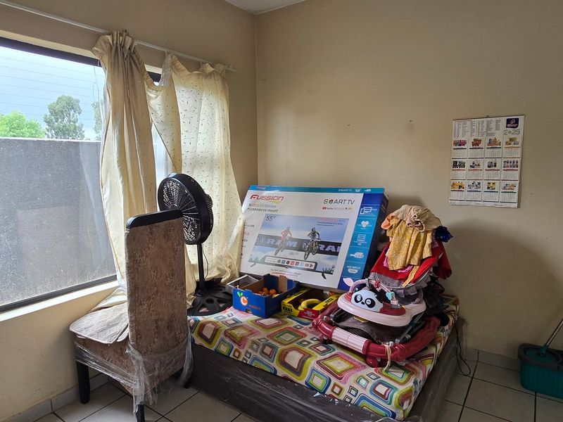 A bedroom featuring tiled flooring and a large window, currently used for storage with visible wear on the wall finishes.