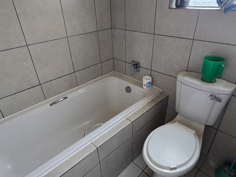 A functional bathroom featuring a standard bathtub, toilet, and full-height wall tiling, presenting a dated but serviceable condition.