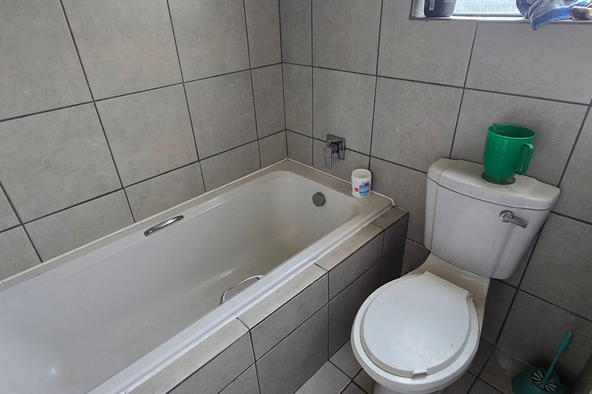 A functional bathroom featuring a standard bathtub, toilet, and full-height wall tiling, presenting a dated but serviceable condition.