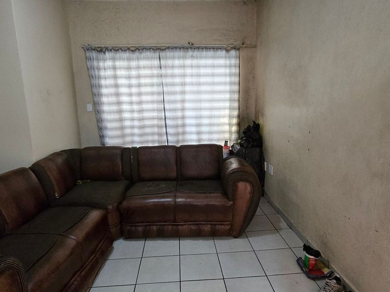 A living room area featuring tiled flooring and wall-mounted electrical fixtures, currently showing significant signs of wear and wall discoloration.
