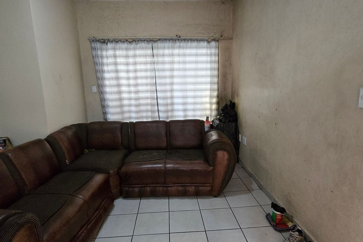 A living room area featuring tiled flooring and wall-mounted electrical fixtures, currently showing significant signs of wear and wall discoloration.