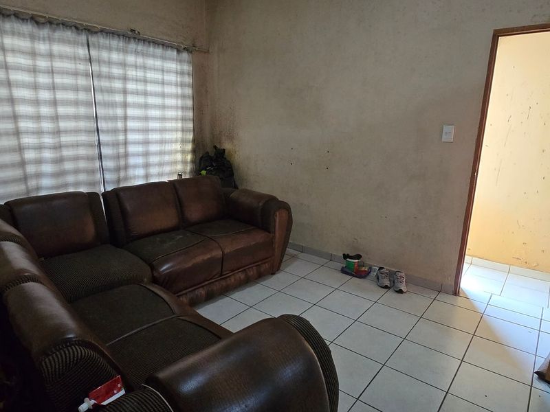 A living room area featuring tiled flooring and a window with a curtain rail, currently requiring wall repairs and repainting.