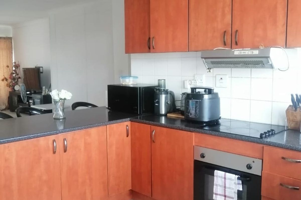 A functional kitchen featuring wood-tone cabinetry, dark laminate countertops, tiled backsplash, and integrated cooking appliances with ceramic floor tiles.