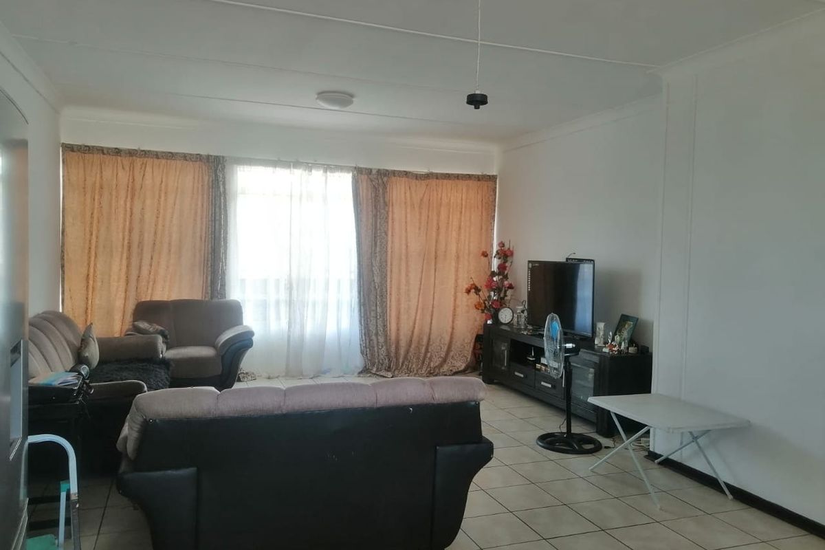 A spacious living room featuring neutral tiled flooring and large windows with curtains, providing ample natural light and a comfortable layout.