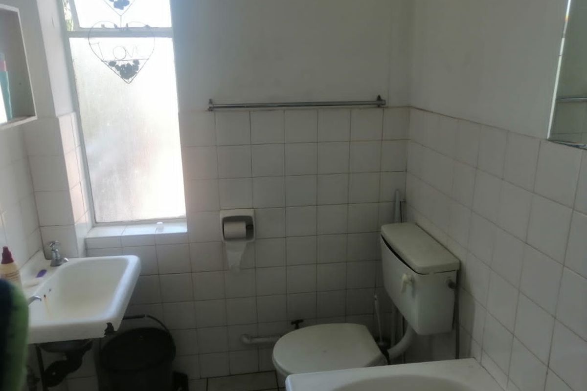 A dated bathroom featuring a wall-mounted basin, standard toilet, and white ceramic wall tiling, requiring cosmetic updates to improve its overall condition.
