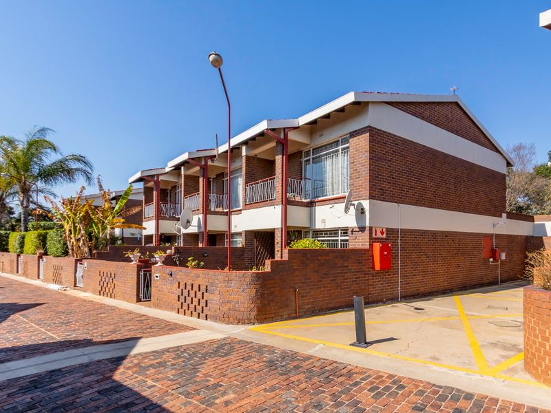 Exterior view of a multi-story townhouse complex featuring face-brick construction, private balconies with metal railings, and a paved driveway area.