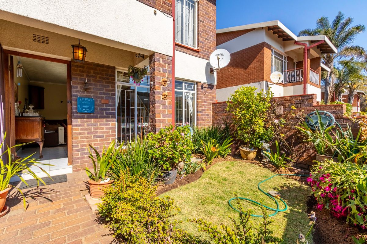 A well-maintained rear townhouse exterior featuring a private garden, paved patio area, and brick facade with secure access.