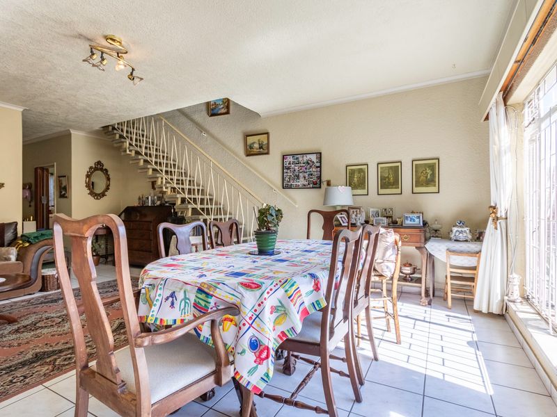 Open plan living and dining area featuring tiled flooring, a central staircase with metal balustrade, and large windows with security gates.
