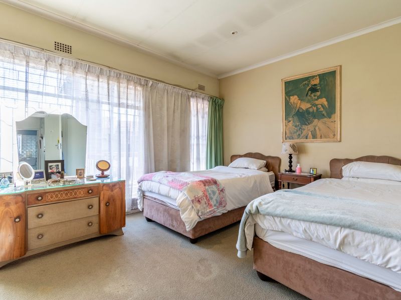 A spacious bedroom featuring neutral wall tones, carpeted flooring, and large windows with curtain tracks, offering a comfortable and functional living space.