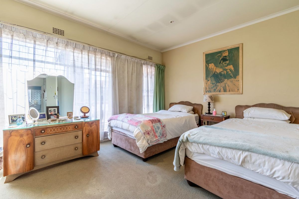 A spacious bedroom featuring neutral wall tones, carpeted flooring, and large windows with curtain tracks, offering a comfortable and functional living space.