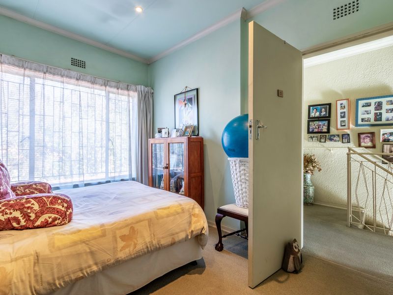 A bedroom featuring light blue walls, crown molding, and a window with security bars, leading out to a hallway with a staircase.