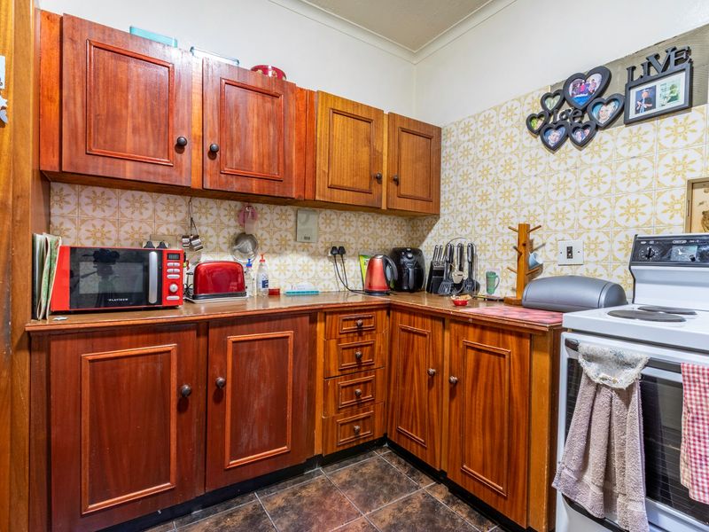 A compact kitchen featuring traditional wooden cabinetry, tiled backsplash, and a freestanding stove, offering a functional layout with potential for modern updates.