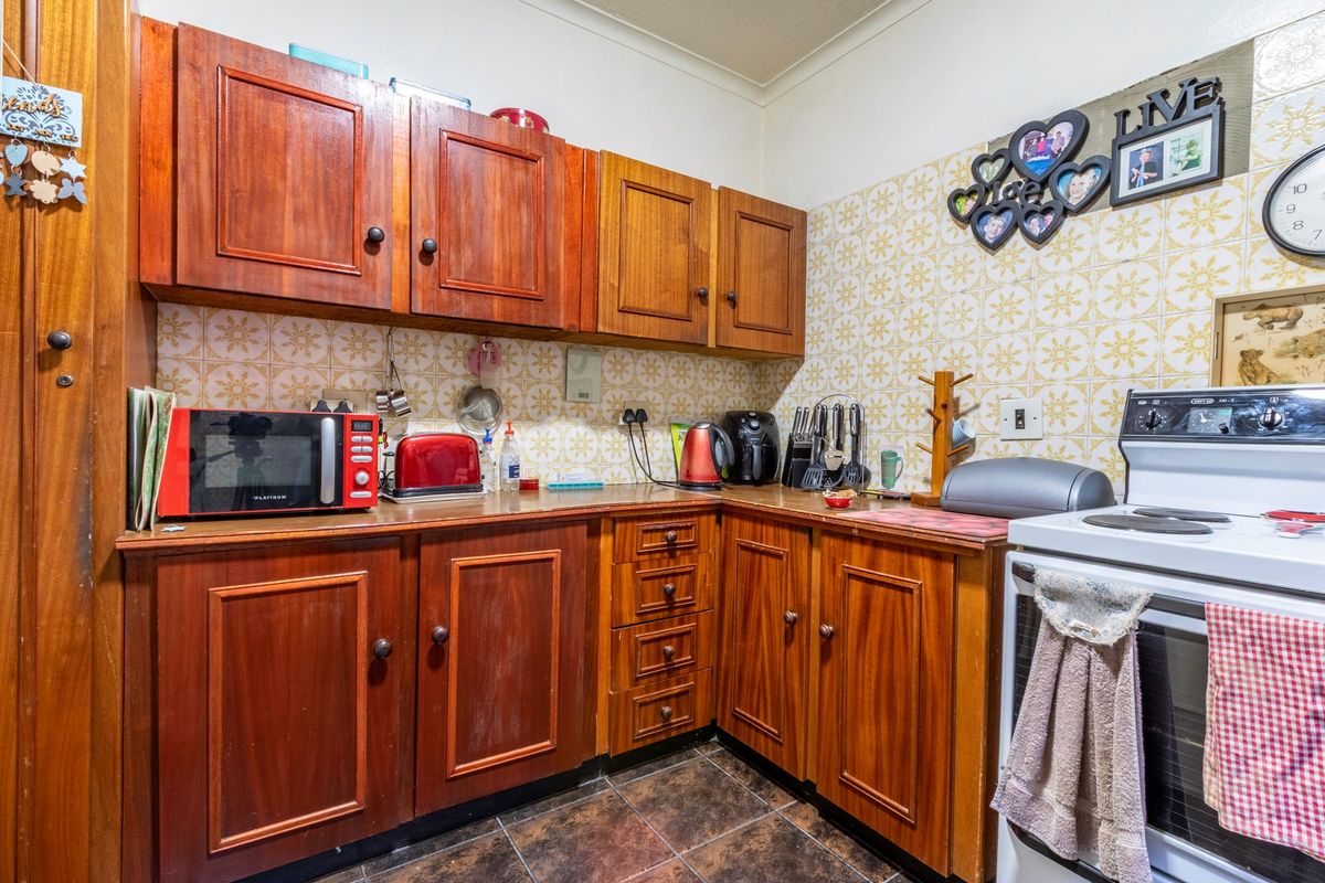 A compact kitchen featuring traditional wooden cabinetry, tiled backsplash, and a freestanding stove, offering a functional layout with potential for modern updates.
