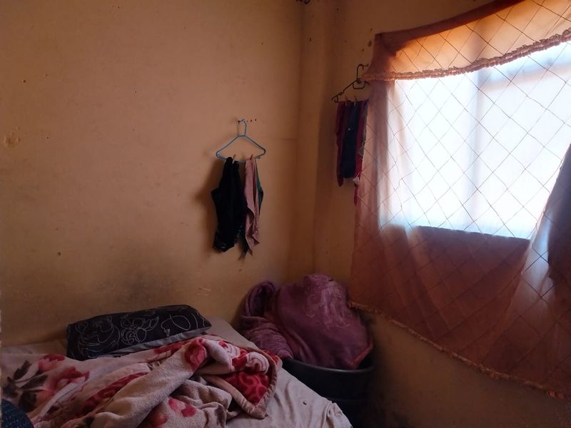 A small bedroom space featuring a window with curtains, showing significant signs of wear and requiring cosmetic updates to the wall finishes.