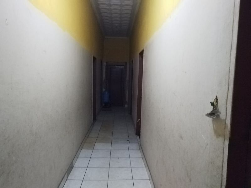 A narrow interior hallway featuring tiled flooring and textured ceiling, currently in need of cosmetic repairs and fresh paint to improve its overall condition.