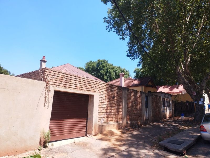 Street-level view of the property featuring a brick boundary wall, a roller shutter garage door, and visible roof structures.