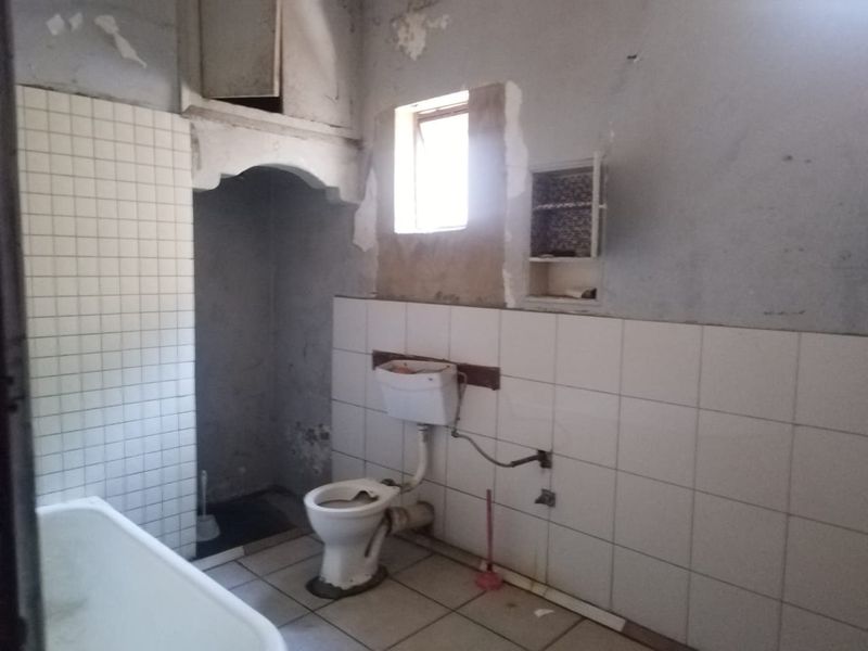 A dilapidated bathroom requiring significant renovation, featuring a bathtub, toilet, and partial wall tiling with visible damage to wall surfaces and plaster.