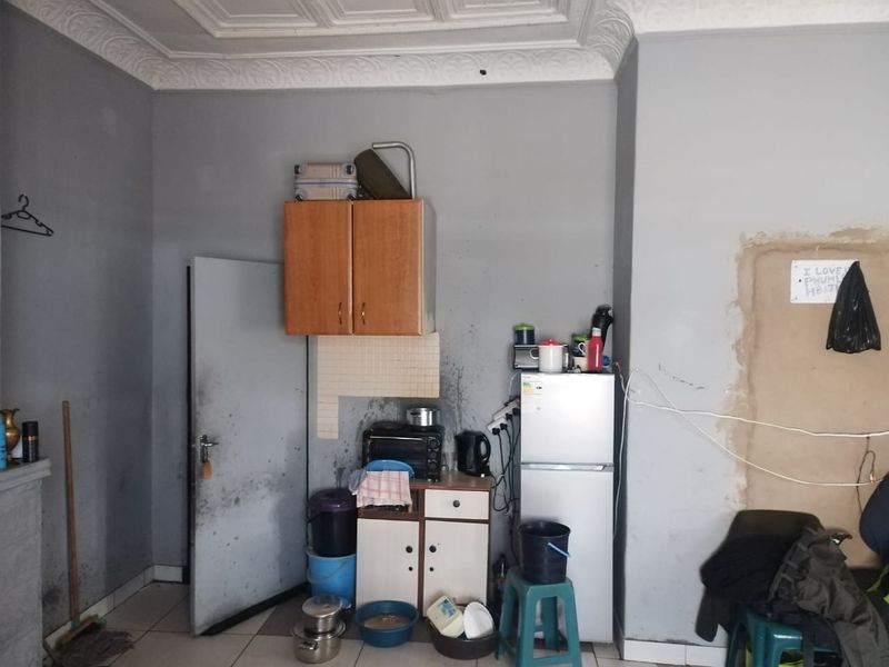 A small kitchen area featuring basic cabinetry, tiled splashback, and tiled flooring, currently requiring significant maintenance and cosmetic updates to improve its condition.