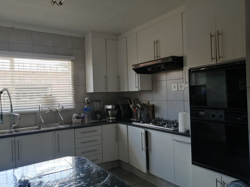 A functional kitchen featuring white cabinetry, granite countertops, a gas hob, extractor fan, and built-in oven with tiled backsplash and sink area.