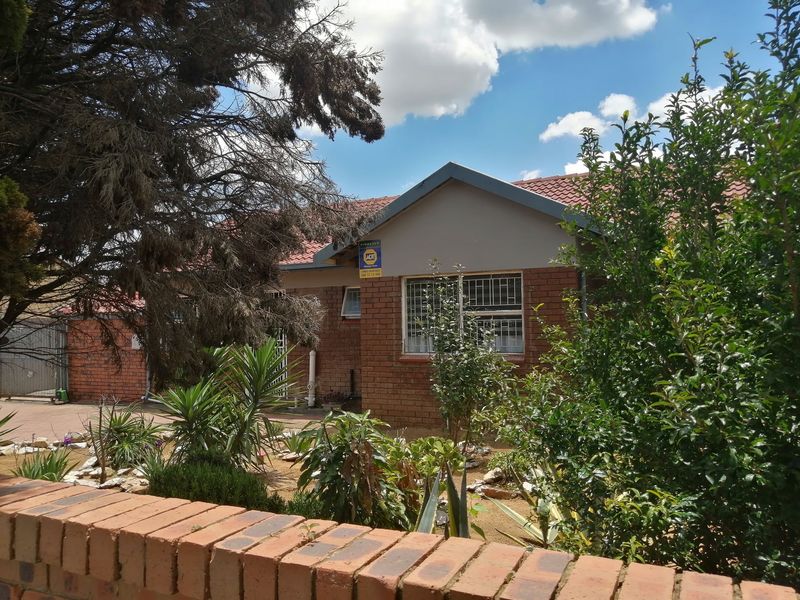 Front elevation of a single-story brick house featuring a tiled roof, security bars on windows, and a low brick boundary wall.