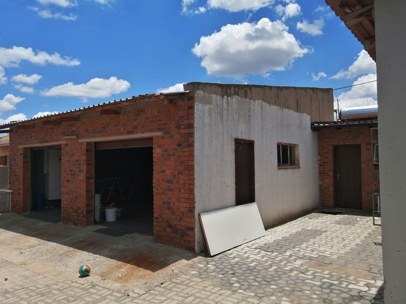 Rear exterior view of a brick structure featuring a paved courtyard, garage access points, and a solar water heating system.