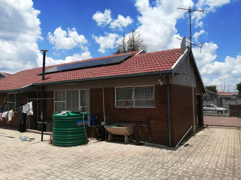 Rear view of a brick house featuring a tiled roof with solar panels, a water storage tank, and paved outdoor area.