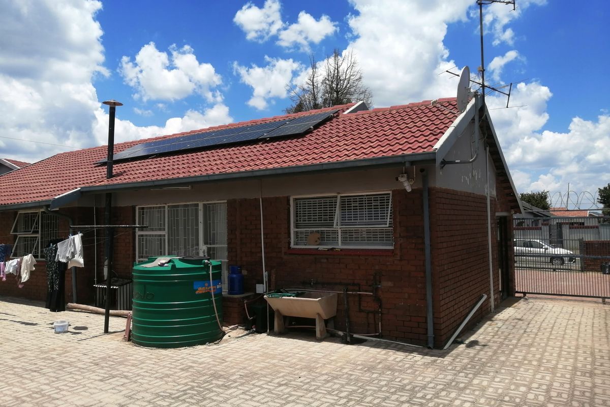Rear view of a brick house featuring a tiled roof with solar panels, a water storage tank, and paved outdoor area.