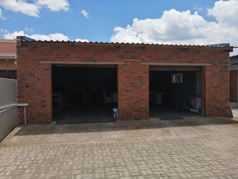 A detached double garage featuring exposed brick construction and a corrugated metal roof, situated on a paved driveway.
