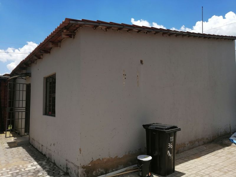 Rear exterior view of the property showing a tiled roof, security gate, and paved area with visible signs of exterior wall maintenance required.