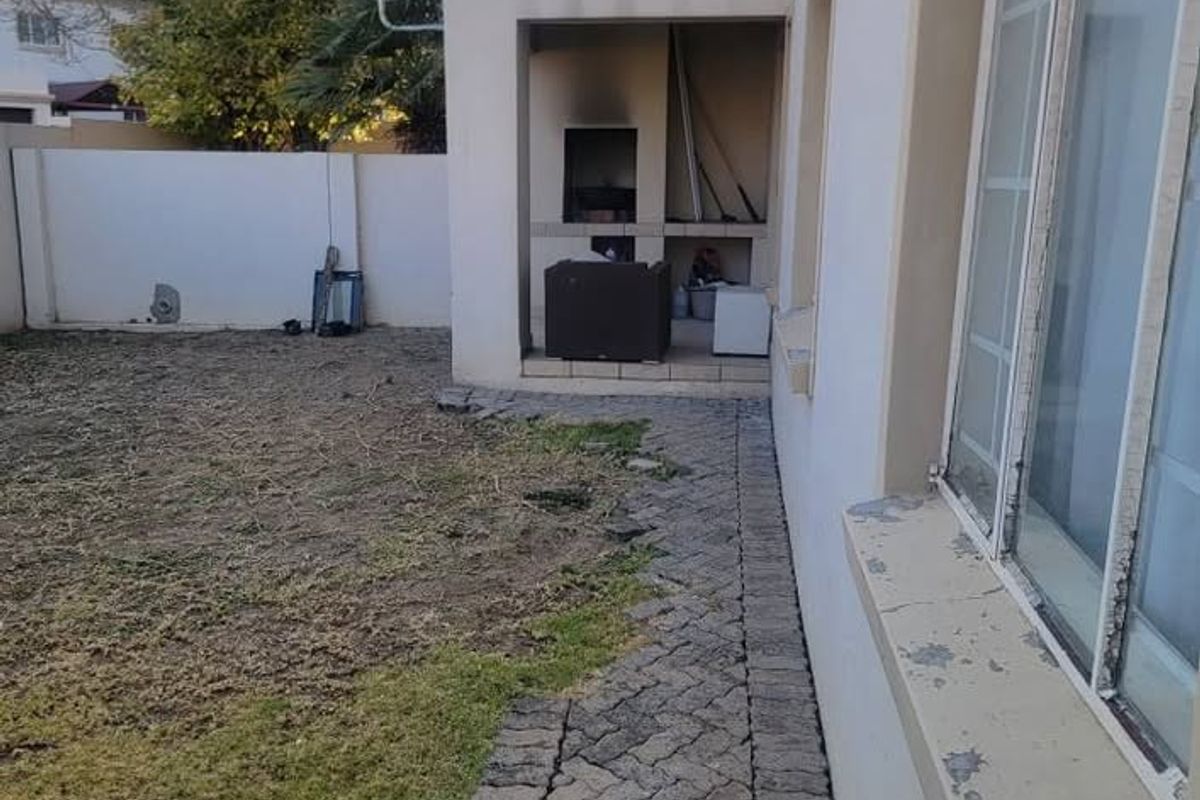 Rear exterior view of the townhouse featuring a paved walkway, a built-in braai area, and an upper-level balcony.