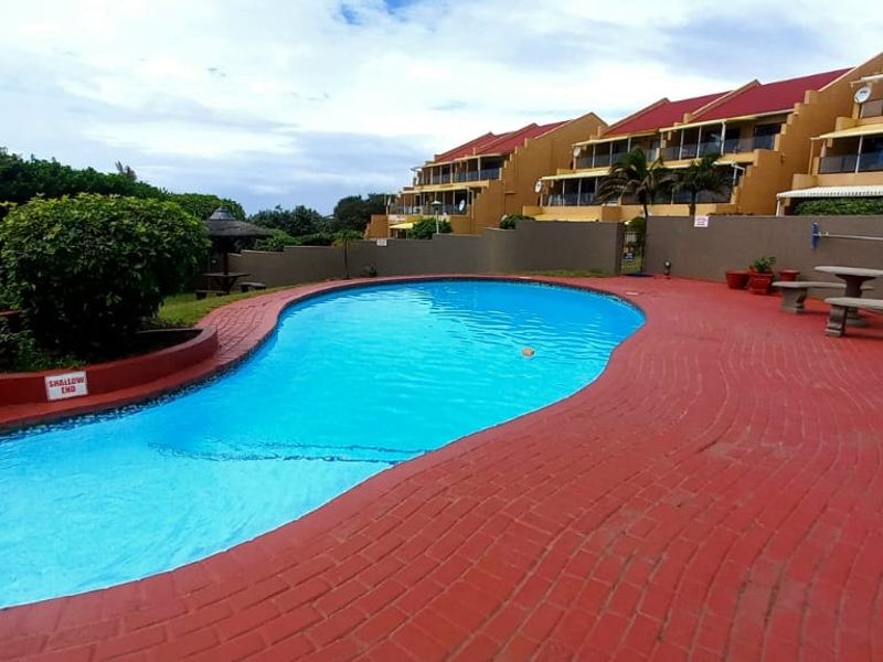 A communal swimming pool area featuring brick paving, a pool handrail, and a view of the apartment complex exterior.