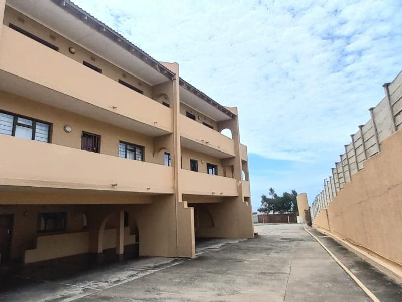 Exterior view of the apartment building featuring multi-level balconies, a paved driveway area, and a high concrete boundary wall.