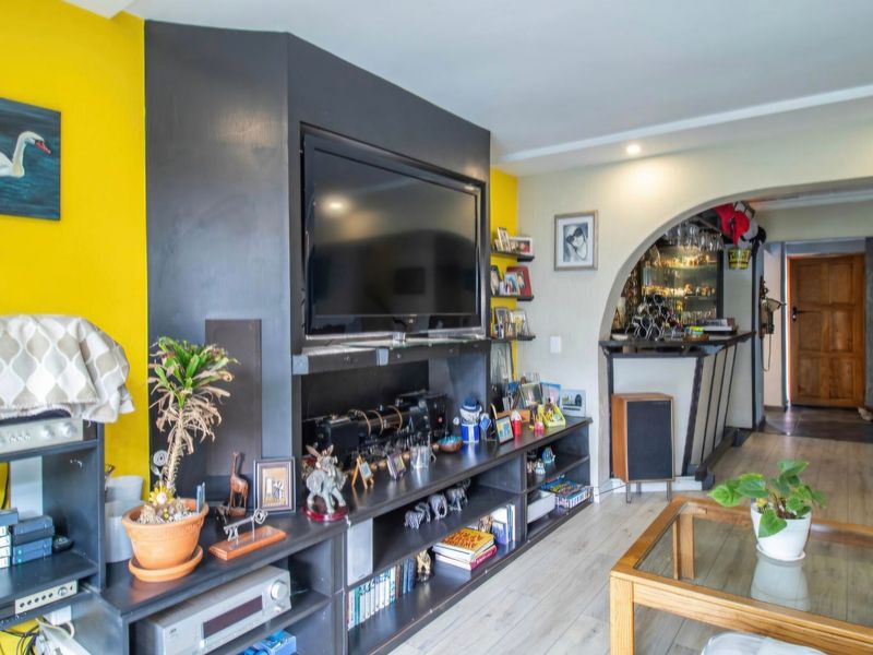Living room featuring a built-in media unit, laminate flooring, and an arched entryway leading to a bar area.