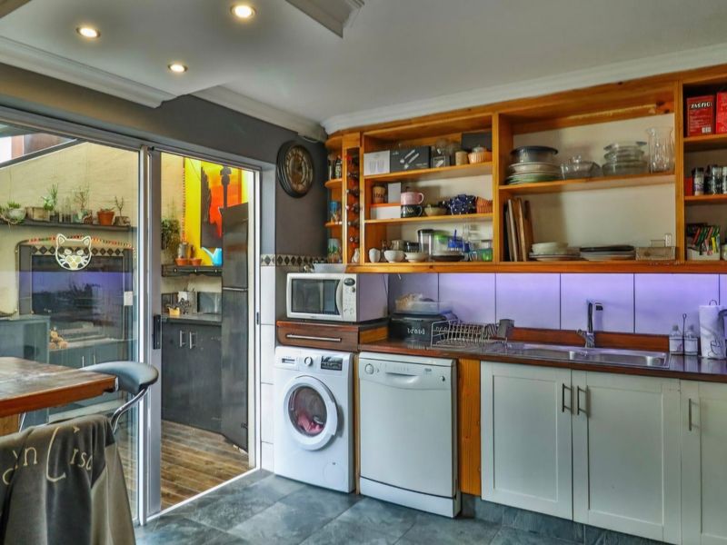A functional kitchen featuring built-in cabinetry, open shelving, and a tiled backsplash, with direct access to an adjacent utility area through sliding glass doors.