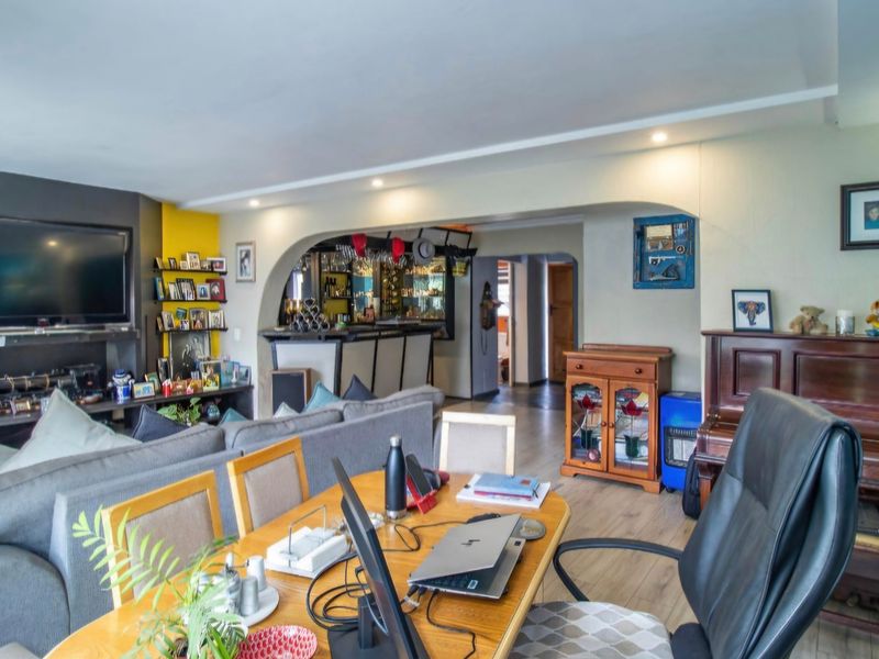 Open plan living and dining area featuring laminate flooring, recessed lighting, and a built-in bar counter with an arched transition to the hallway.