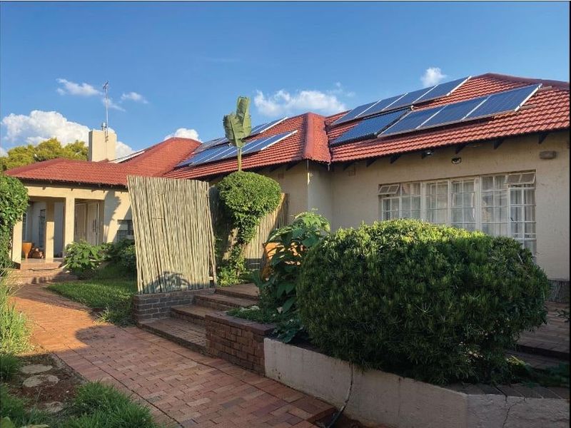 Rear view of the house featuring a tiled roof with installed solar panels, brick paved pathways, and landscaped garden areas.
