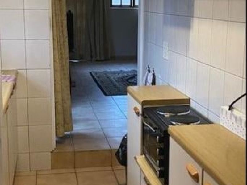 A compact kitchen featuring tiled walls and flooring, built-in cabinetry, and an electric stove, requiring modernization to improve functionality and aesthetic appeal.