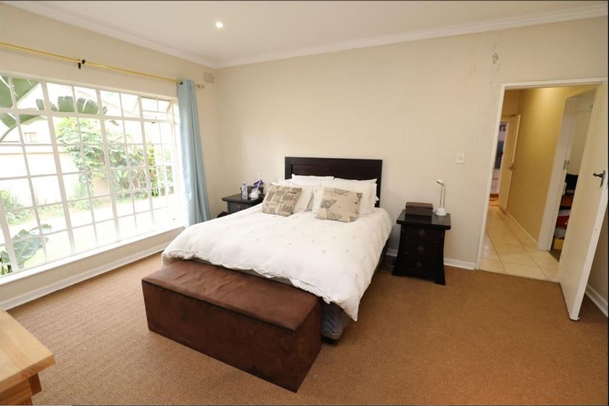 A spacious bedroom featuring large windows, carpeted flooring, and direct access to an adjoining hallway.