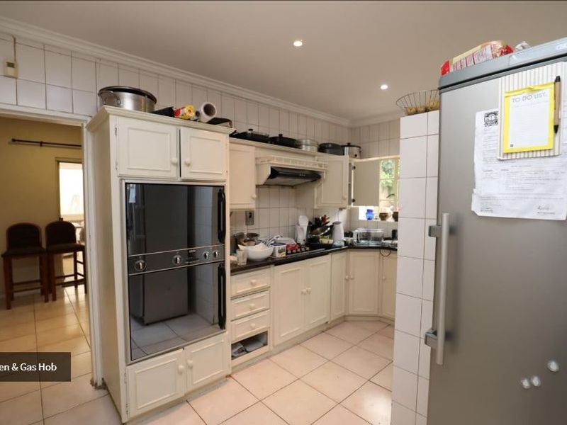 Functional kitchen featuring built-in oven, gas hob, extractor fan, and tiled finishes, offering a practical layout with ample storage cabinetry.