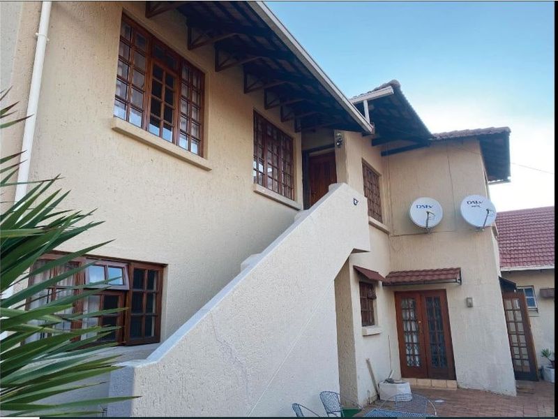 Rear exterior view of a two-story house featuring stucco walls, timber-framed windows, an external staircase, and a paved patio area.