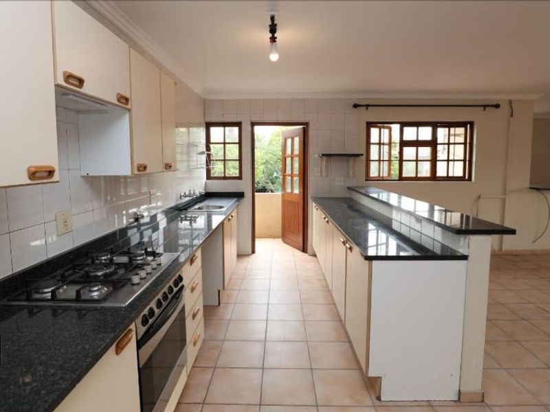 Spacious kitchen featuring granite countertops, gas hob, built-in oven, and a breakfast bar, with direct access to an outdoor area.