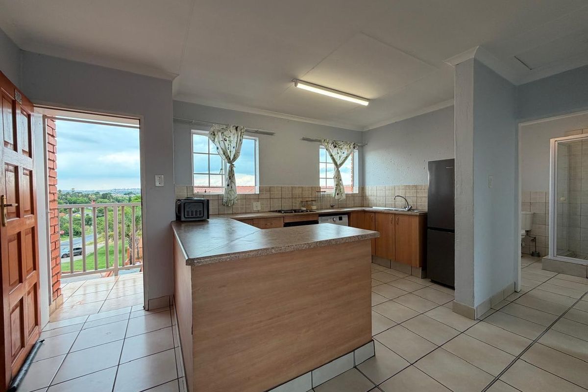 Open-plan kitchen featuring laminate cabinetry, tiled countertops, and flooring, with direct access to a balcony area.