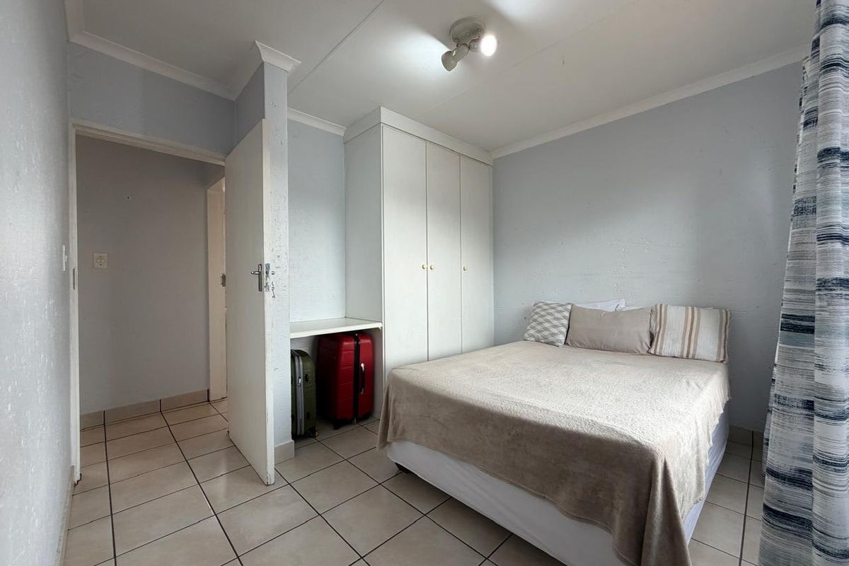 A functional bedroom featuring tiled flooring, built-in cupboards, and a neutral color palette, offering a practical space for rest.