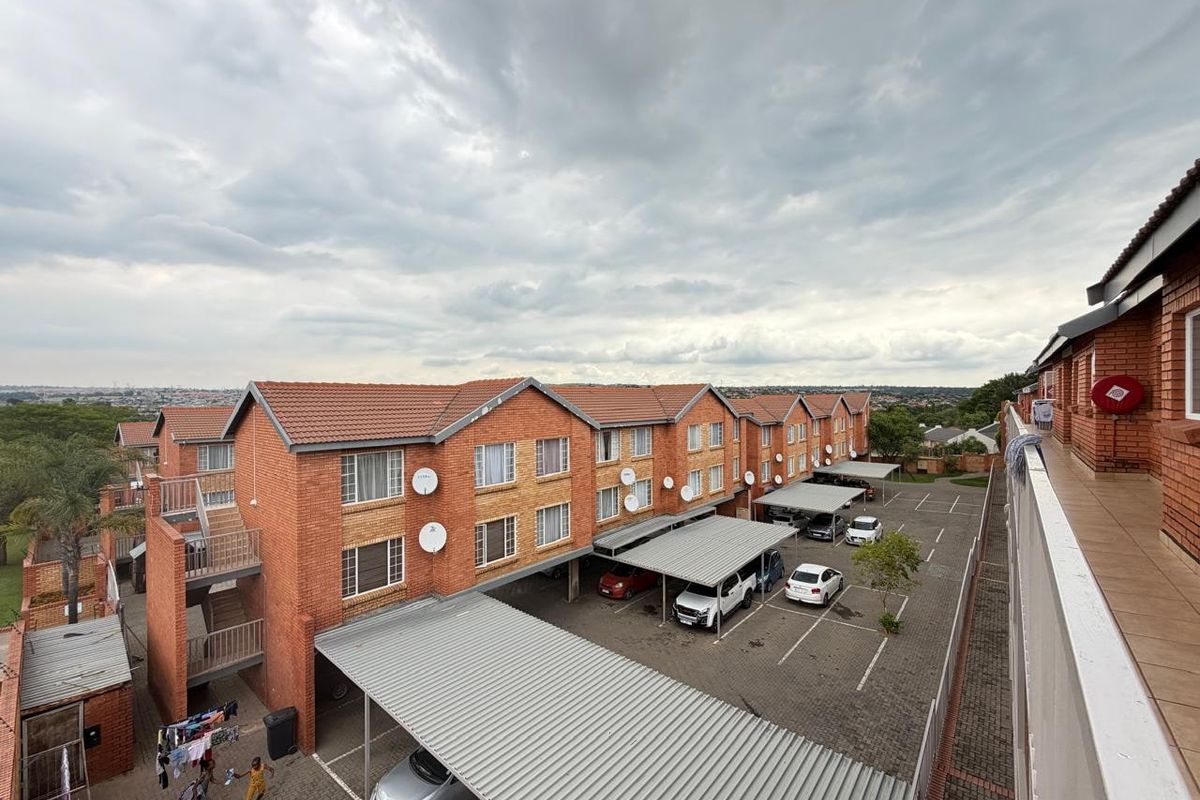 Aerial view of an apartment complex featuring face brick buildings, covered parking bays, and paved communal areas under a cloudy sky.