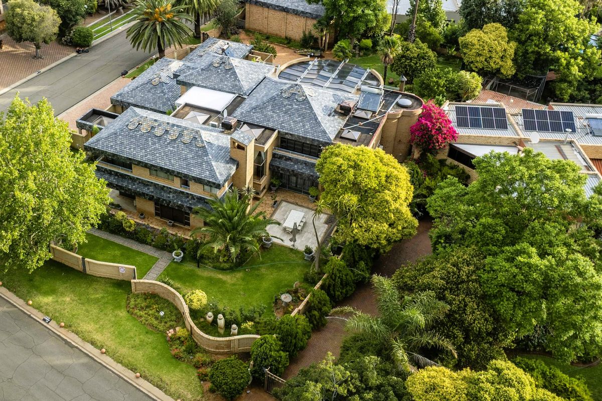Aerial view of a large residential property featuring a multi-level slate roof, integrated solar panels, mature landscaped gardens, and paved driveway access.